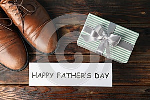 Brown leather shoes, inscription happy fathers day and gift box on wooden background, space for text