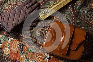 Brown leather vintage bag on background with flowers and abstract patterns, brown gloves and vintage leather bag top view