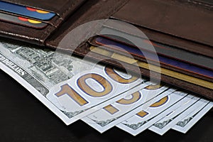 Brown leather wallet full of 100 USD bills on black table.