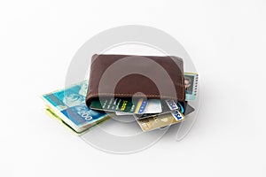 Brown leather wallet and several credit cards, club cards and stack of banknotes new Israeli shekels isolated on white background