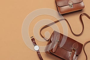 Brown leather women bag, stylish wristwatch on brown beige background top view flat lay copy space. Fashionable women`s