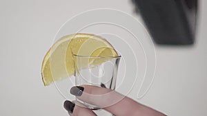 Brown liquid is being poured on glass with lemon held by woman`s hand