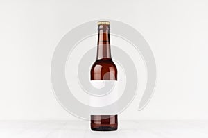 Brown longneck beer bottle 330ml with blank white label on white wooden board, mock up.