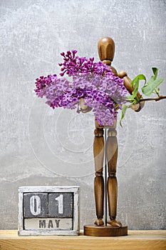 Brown mannequin holds sprig of lilac next wooden calendar with date May 01.