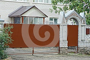 Brown metal closed gate and part of a brick fence in the street