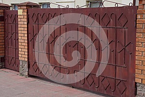 Brown metal gate with forged pattern and brick fence in the street