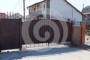 Brown metal gate with a forged pattern and part of the fence on the street