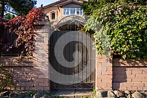 A brown metal gate in a pink brick fence. Entrance from the street