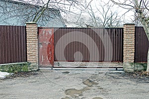 Brown metal gate and red closed door on a fence made of iron