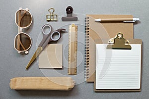 Brown notebook, clipboard, pen, ruler, clip, memopad, pencil case, scissors, eyeglasses on gray desk background photo