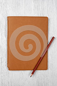 Brown notebook and a pencil on white wooden table, top view