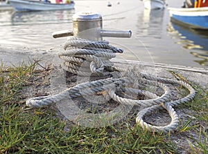 Brown old anchor rope wrapped around dock pier post. Anchor rope in the port, ship mooring tool. Close-up of textile rope on a