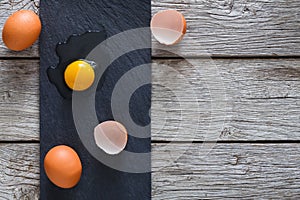 Brown organic cracked eggs with yolk on black wood background