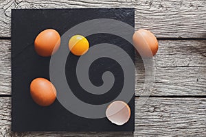 Brown organic cracked eggs with yolk on black wood background