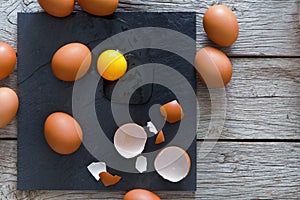 Brown organic cracked eggs with yolk on black wood background