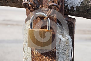 A brown padlock hanging on a rusty iron chain