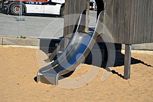 Brown painted wooden house on a playground with a sandpit. stainless steel slides shine in the sandy beach. wooden benches separat