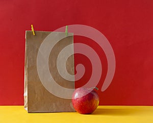 Brown paper bag and a red apple on colorful paper background