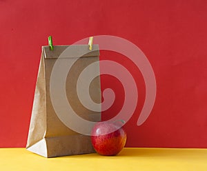 Brown paper bag and a red apple on colorful paper background