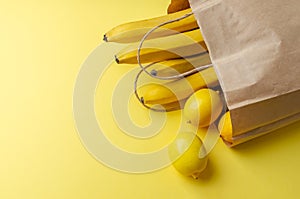 Brown paper bag with yellow fruits. Bananas and lemons falling out of a paper bag on yellow background. Healthy vegan vegetarian
