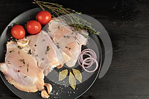 On brown paper, fresh skinless chicken thighs, next to mushrooms, with tomatoes, red onions and thyme. Recipe of dish. Ingredients