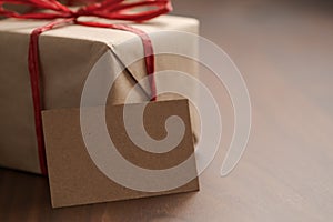 Brown paper gift boxes with red bow and blank paper card on walnut table with copy space