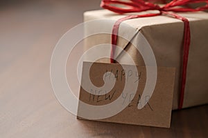 Brown paper gift boxes with red bow and Happy New Year paper card on walnut table with copy space