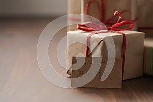 Brown paper gift boxes with red bow and Happy New Year paper card on walnut table with copy space