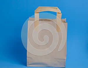 brown paper shopping bag on blue background. Brown empty craft lunch bag. Recycle brown paper bag.