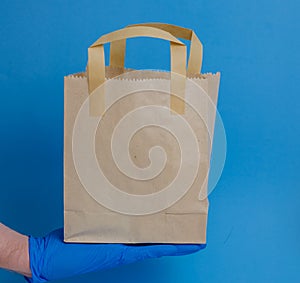 brown paper shopping bag on blue background. Brown empty craft lunch bag. Recycle brown paper bag. Hand in glove holding