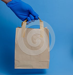 brown paper shopping bag on blue background. Brown empty craft lunch bag. Recycle brown paper bag. Hand in glove holding