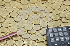 Brown pencil with black calculator on stack of gold coins