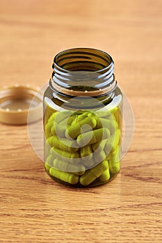 Brown plastic vial with white pills on wooden background