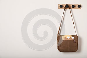 Brown postman bag with mails hanging on light wall, space for text