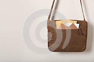 Brown postman bag with mails hanging on light wall, space for text