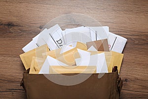 Brown postman bag with newspapers and mails on wooden table, flat lay