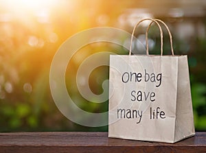 Brown recyclable paper shopping bag Placed on a wooden table, the backdroup is a green tree.