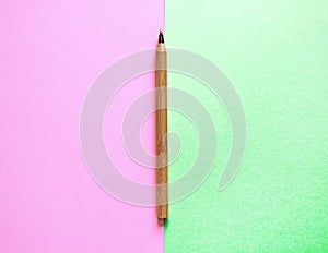 Brown recycled eco pen on the edge of two backgrounds: pink and green