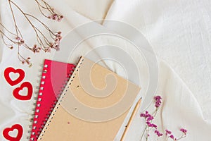 Brown and red notebooks with red flowers on white fabric.