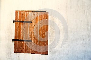 Brown red wooden window with rusted metal hinges on a white cement wall detail.