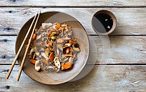 Brown rice noodles with fried chicken and carrots on natural wooden table