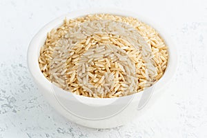 Brown rice in white bowl on white background. Dried cereals in cup, vegan food, fodmap diet. Side view, close up