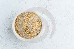 Brown rice in white bowl on white background. Dried cereals in cup, vegan food, fodmap diet. Top view, close up