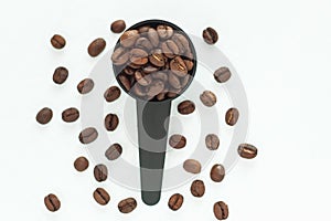 Brown roasted coffee beans in a black measuring spoon on a white background isolated