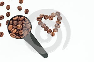 Brown roasted coffee beans in a black measuring spoon on a white background isolated