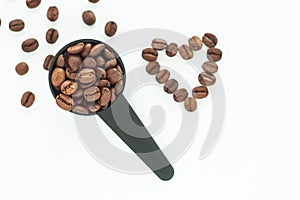 Brown roasted coffee beans in a black measuring spoon on a white background isolated