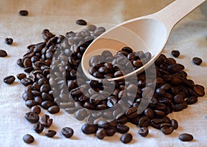 Brown roasted coffee beans and wooden spoon on piece of linen