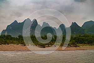 Brown rocky shoreline in front of karst mountains along Li River in Guilin, China