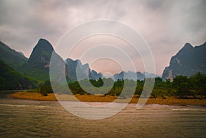 Brown rocky shoreline in front of karst mountains along Li River in Guilin, China