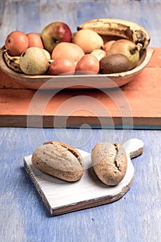 Brown rolls on a wooden chopping board isolated on blue table with a fruit bowl in the background